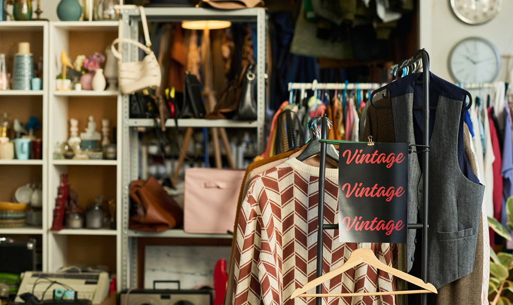 Vintage clothing on rails beside shelves of second-hand bags and homewares